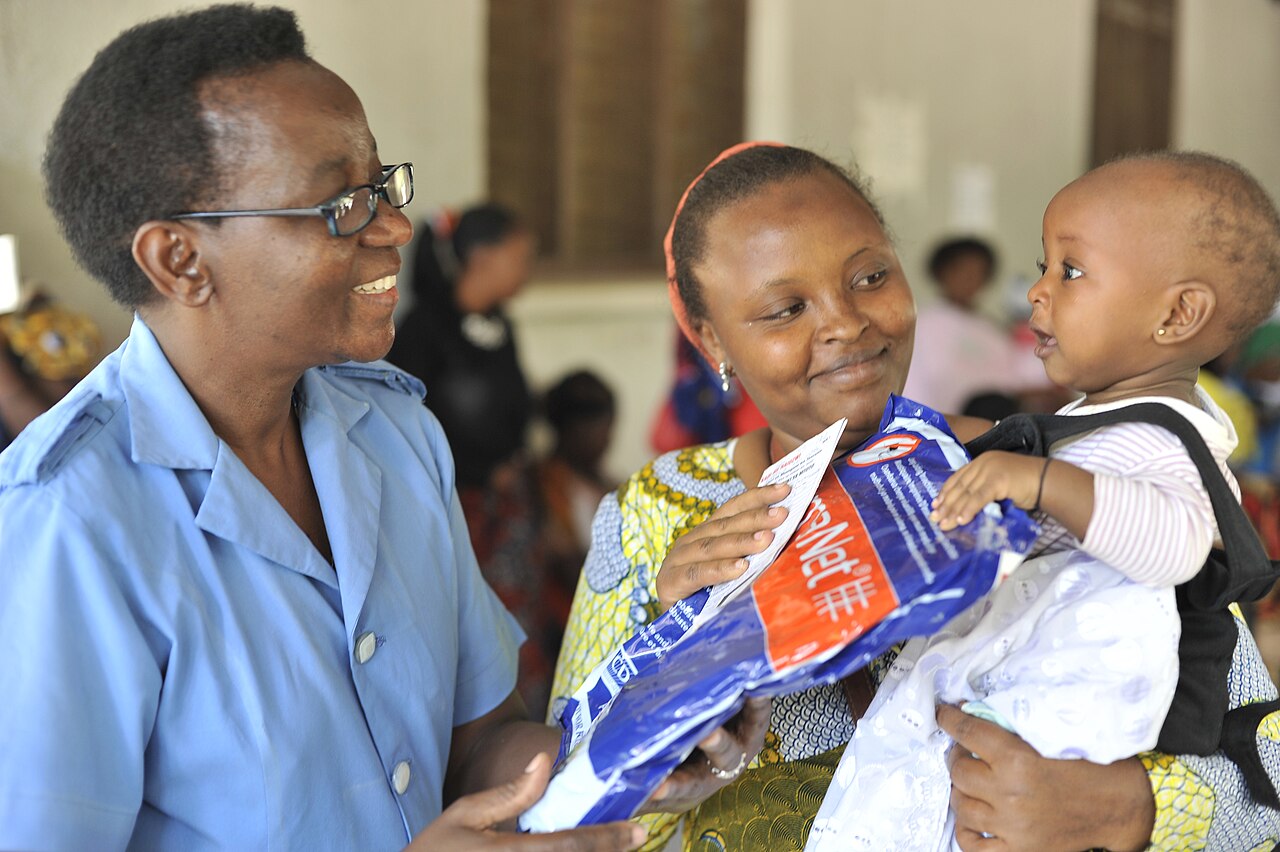 A hospital nurse handing a mosquito net to a mother holding her daughter