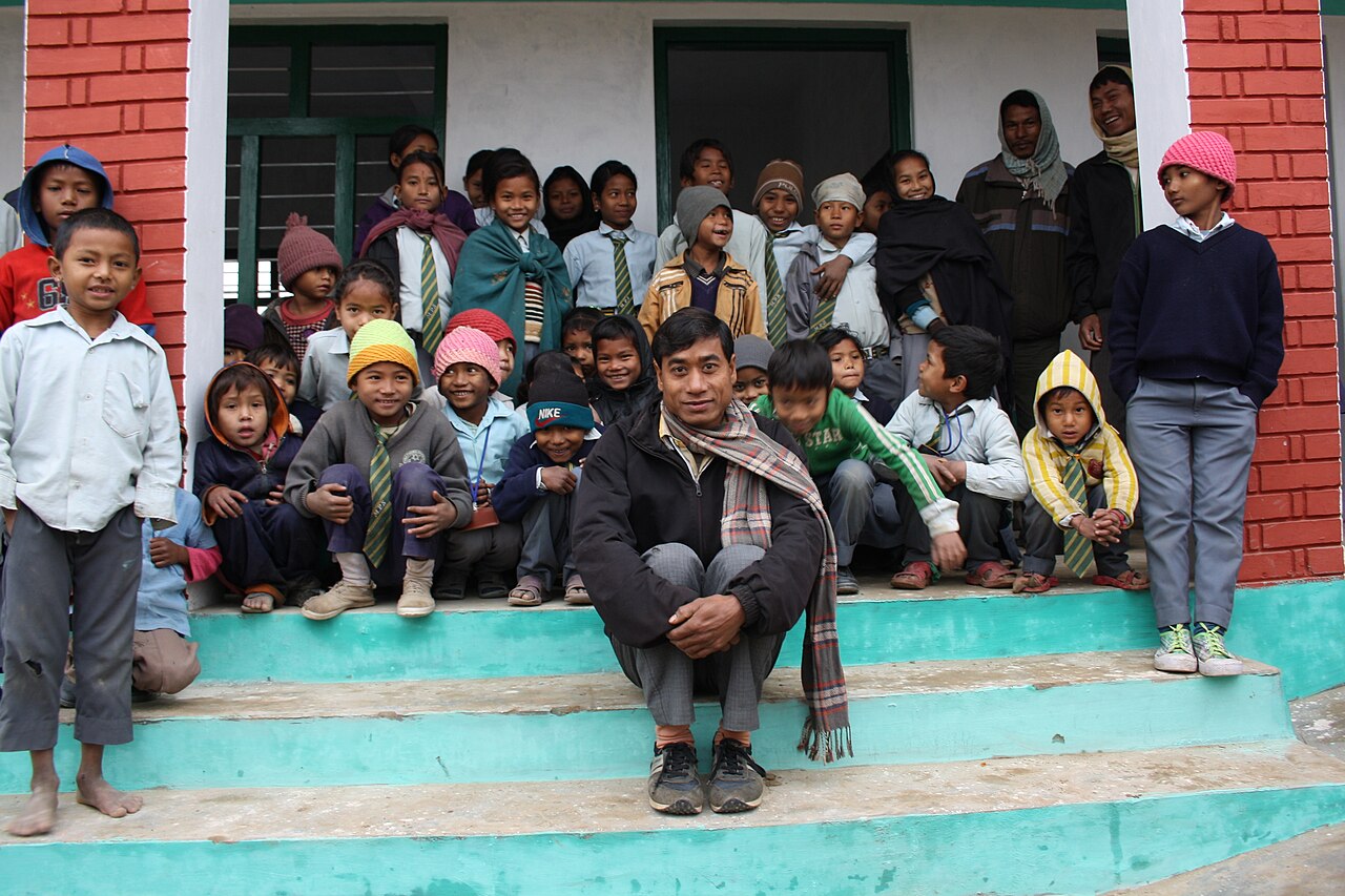 A teacher sitting on the school steps with his pupils in rural Nepal, after their old classroom was destroyed