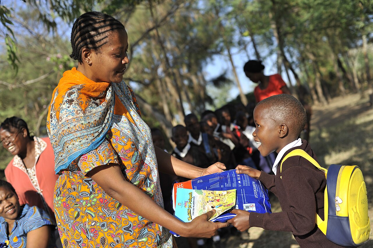 A primary school teacher handing a mosquito net to a seven year old pupil outside her school