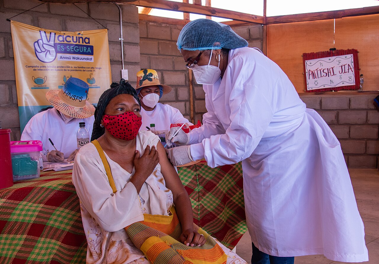 A health worker vaccinating a woman at a mobile clinic with breeze block walls